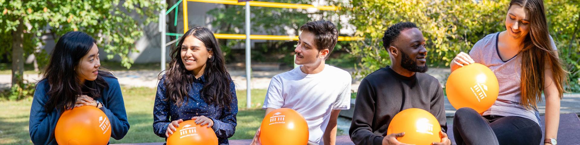 Foto zeigt fünf Studierende mit einer stw Berlin Ball draußen sitzend und in die Kamera lächelnd