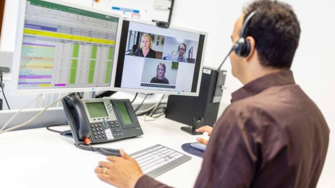 Sachbearbeiter am Arbeitsplatz mit zwei Bildschirmen in einem Online-Meeting.