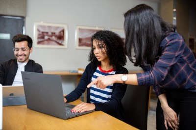 A writing tutor helps two students write on a PC.