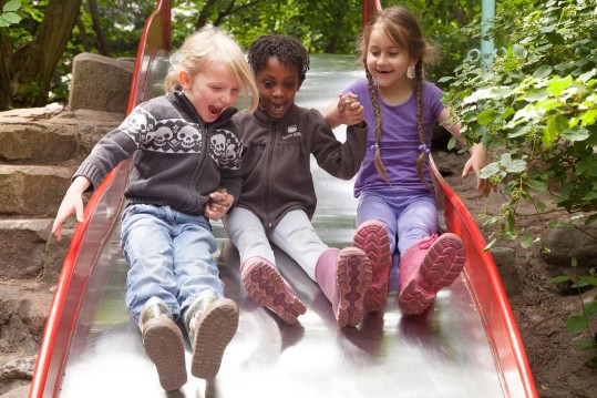 Drei Kleinkinder rutschen begeistert eine breite Rutsche hinunter.