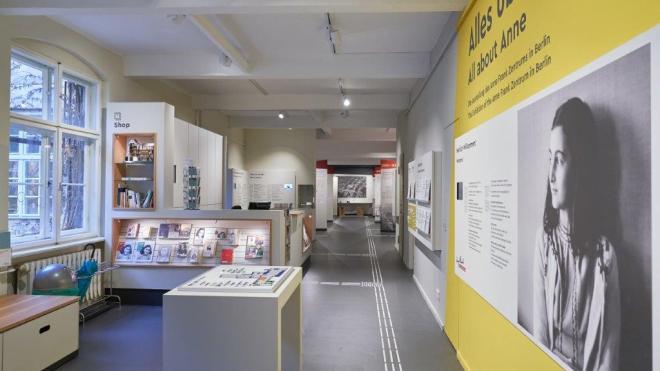 Insight into the exhibition: On the right, a wall with a picture of the young Anne Frank. On the left, shelves with books and exhibits