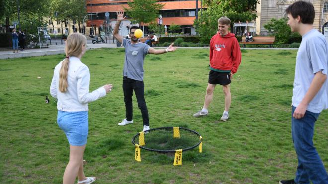 Young people stand around a trampoline and happily throw a small ball to each other.
