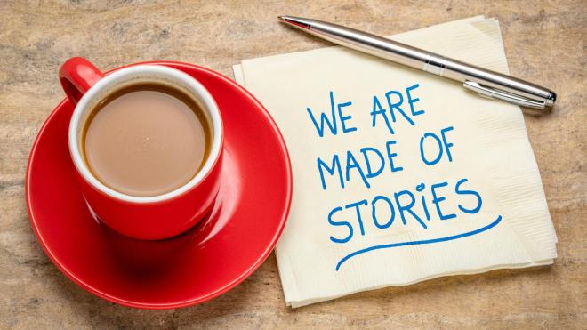 A red coffee cup and a napkin with "We are made of stories" written on it.