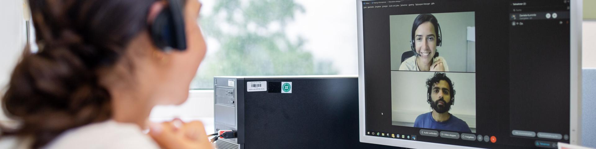 One person wears headphones and talks to two other people who can be seen on a PC screen.