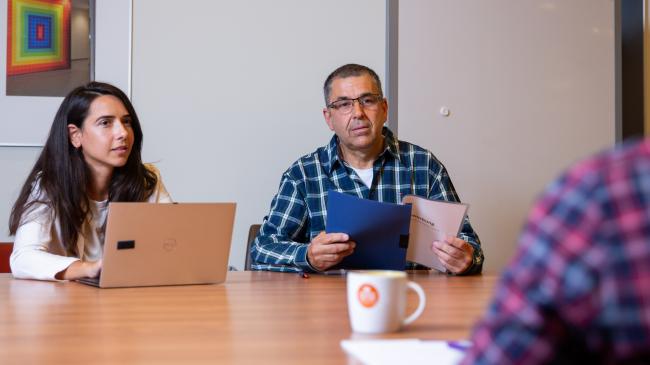 Photo shows applicant who has two interviewers in front of him, one of whom is looking at the application portfolio