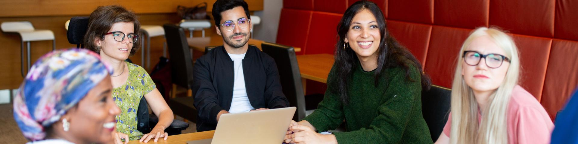Cheerful-looking students at a table in a seminar room. One student is sitting in a wheelchair.
