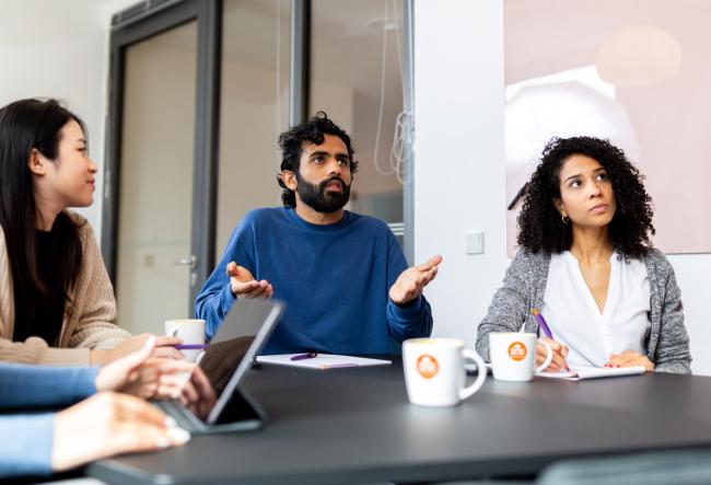 Picture shows three students in a consulting situation. One of them asks questions. 