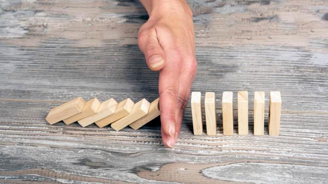 Hand that interrupts a falling row of dominoes in the half from falling further.