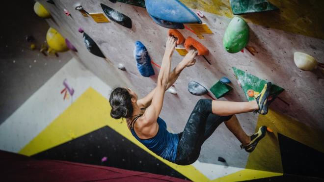 Young woman bouldering: With ease she holds on to a sloping wall